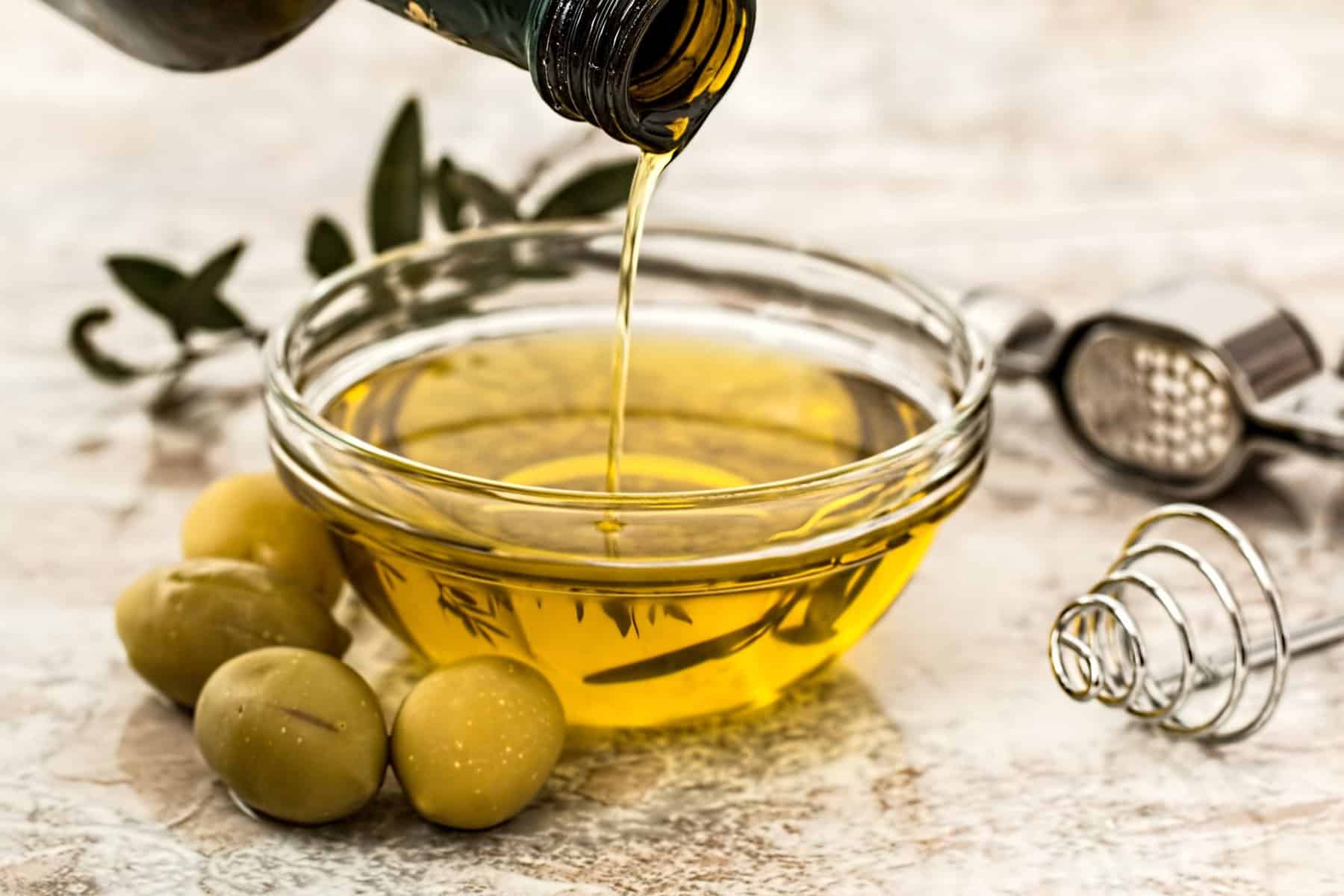 Healthy fat – Olive oil bring poured into small ramekin with olives surrounding the scene